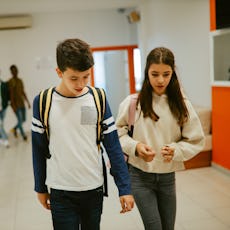 A young teen couple walks together in the hall at school.